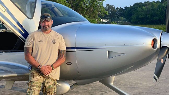 Neuroendocrine tumor survivor Curtis Crump standing in front of a sheriff's department airplane