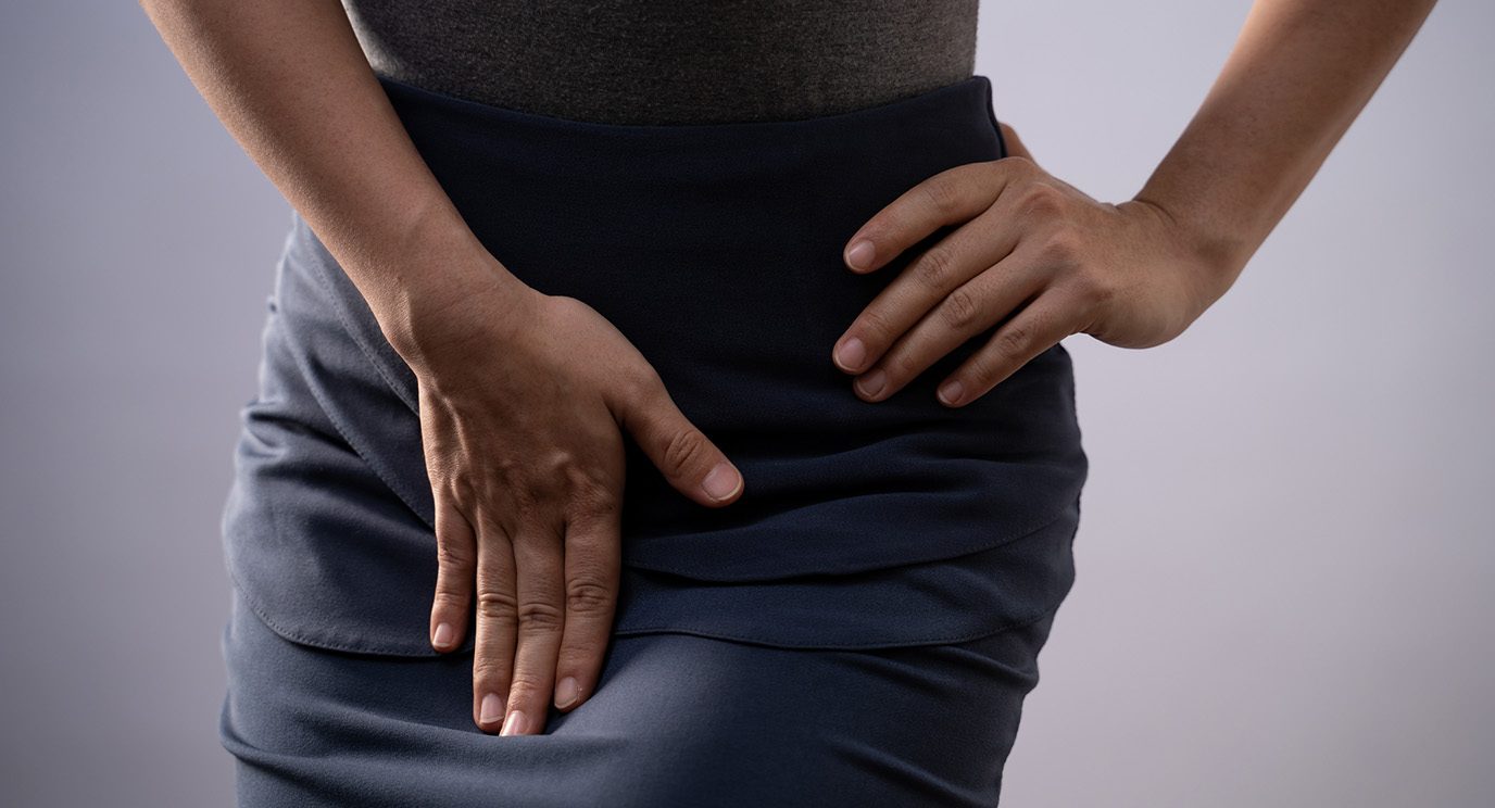 Close-up gray-scale photo of slender woman's waist in pencil skirt with one hand covering groin area