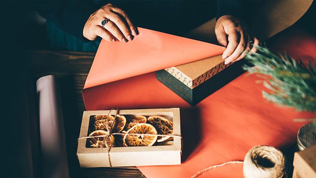 Person wrapping a cardboard gift box in red wrapping paper.