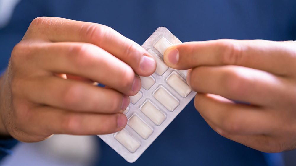 Person in blue shirt holds a packet of white gum in a silver foil package