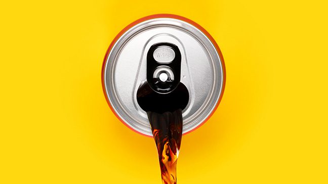 A silver can pours out brown soda against a yellow background.