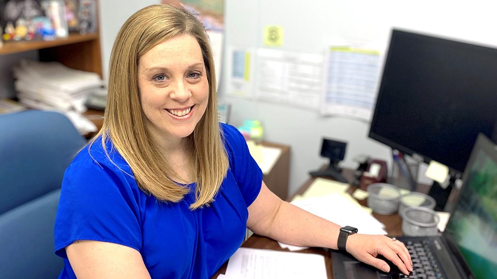 Cervical cancer and total pelvic exenteration survivor Shalee Landry sits at her desk in front of a computer