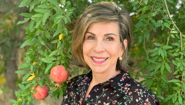 Anal cancer survivor Bibi Philippou smiling in her garden in front of a pomegranate tree