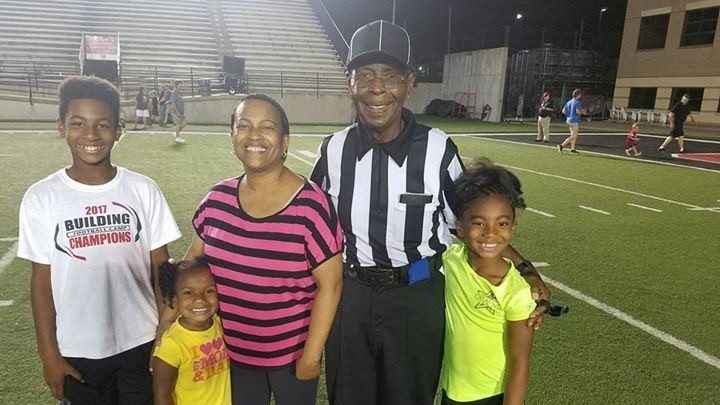 Kidney cancer survivor Primus Moore poses in his referee uniform with his family on a football field