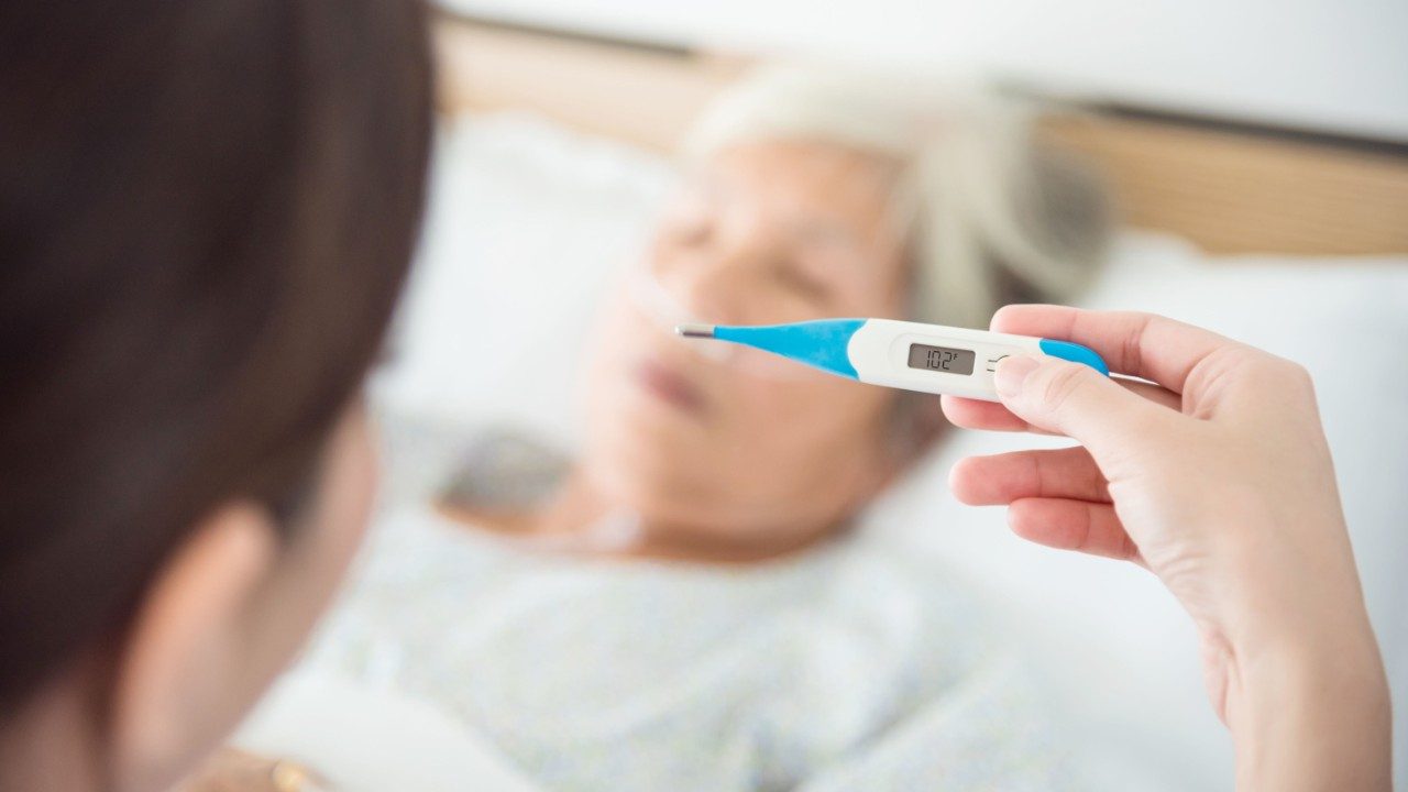 Digital thermometer registering a fever with sick woman in bed in background