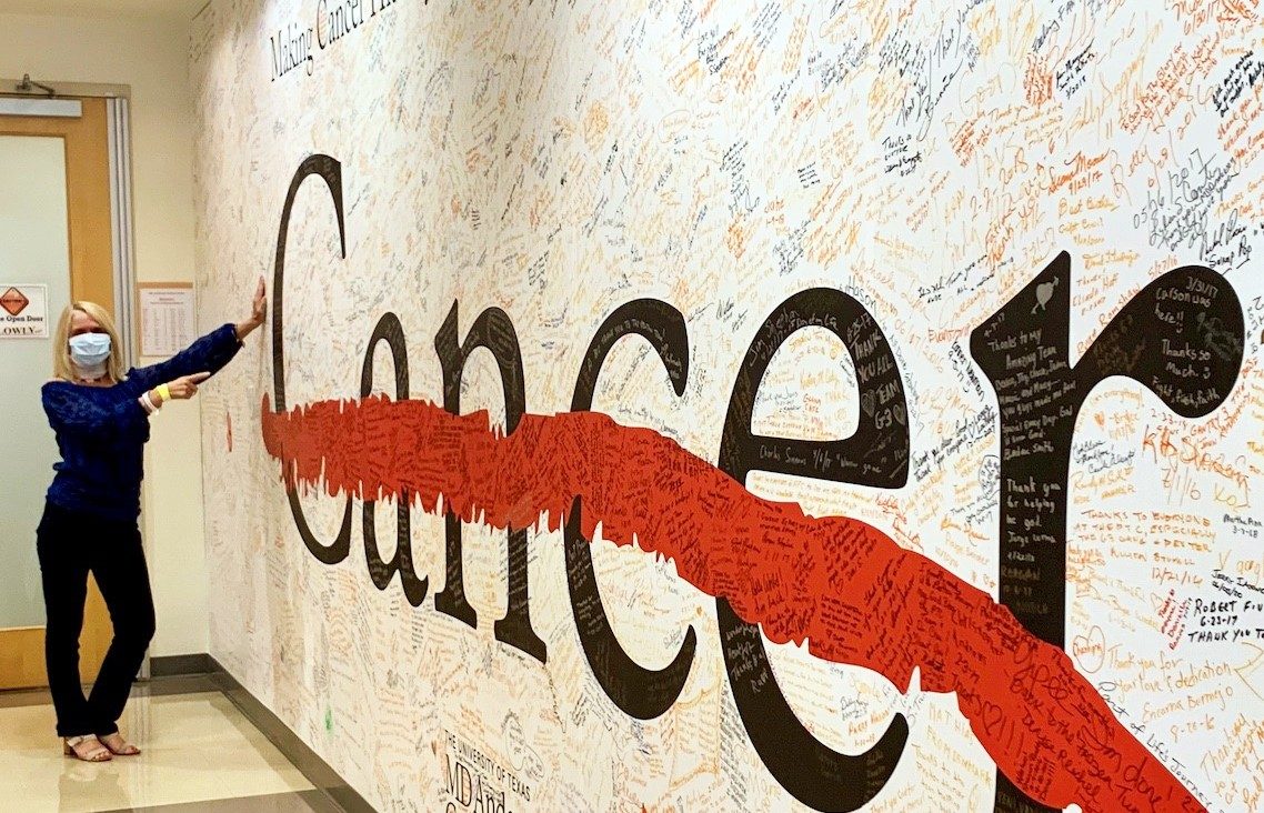 Squamous cell carcinoma survivor Jill Spencer points at the cancer strikethrough wall at the Proton Therapy Center after completing treatment