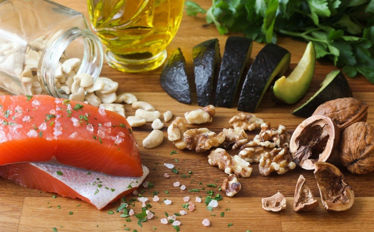 Some ingredients found in teh Meditteranean diet are shown on a board: salmon, walnuts, olive oil and avocado.