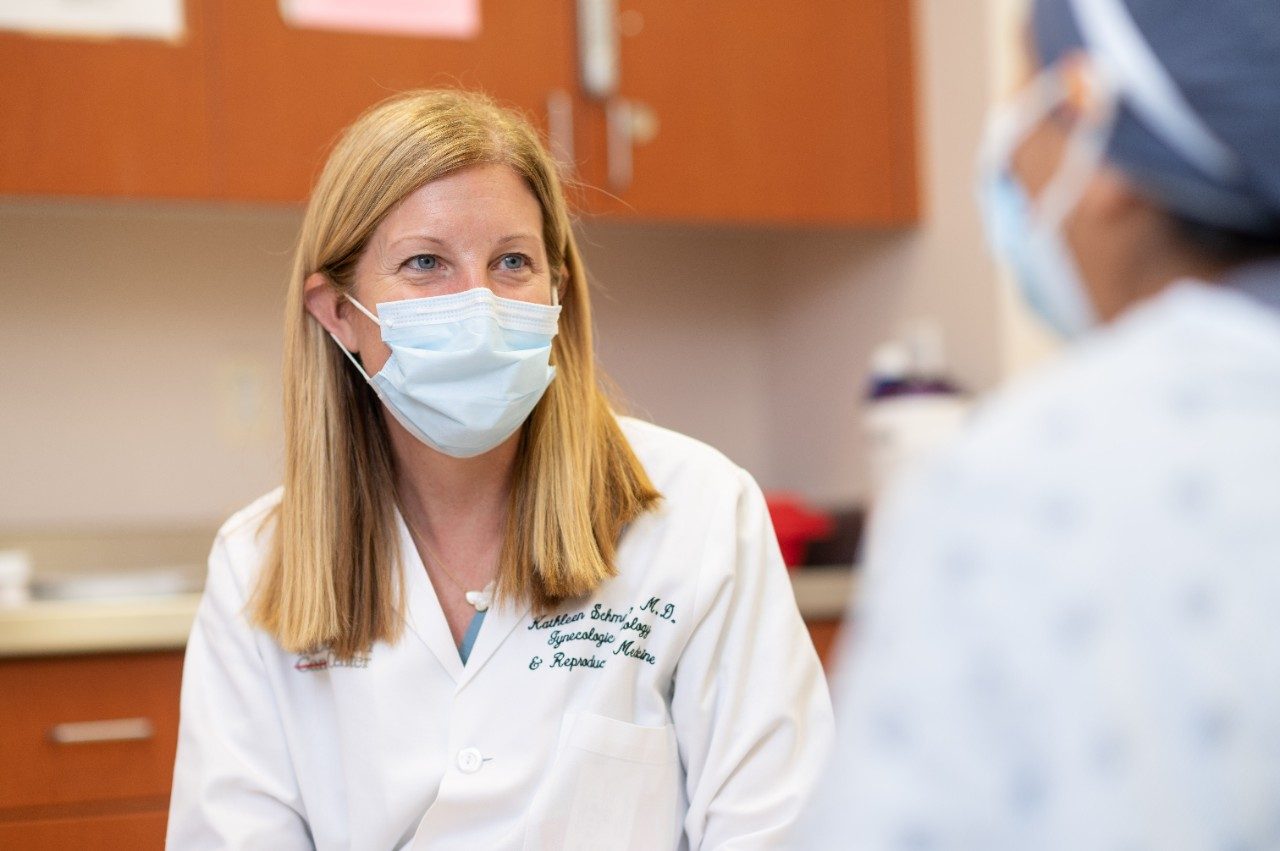 Physician Kathleen Schmeler, M.D., looks at a patient while meeting with her. Both are wearing medical-grade face masks.