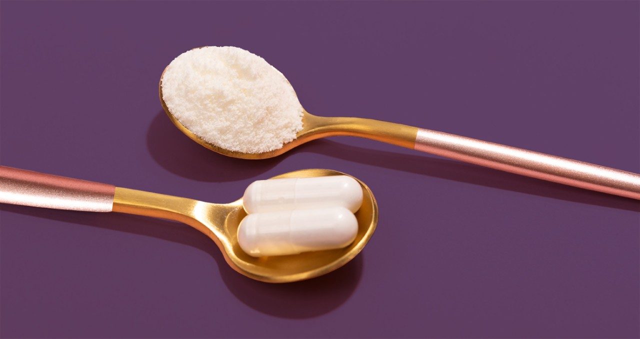 two gold spoons on a purple background, one with white powder and one with white capsule pills