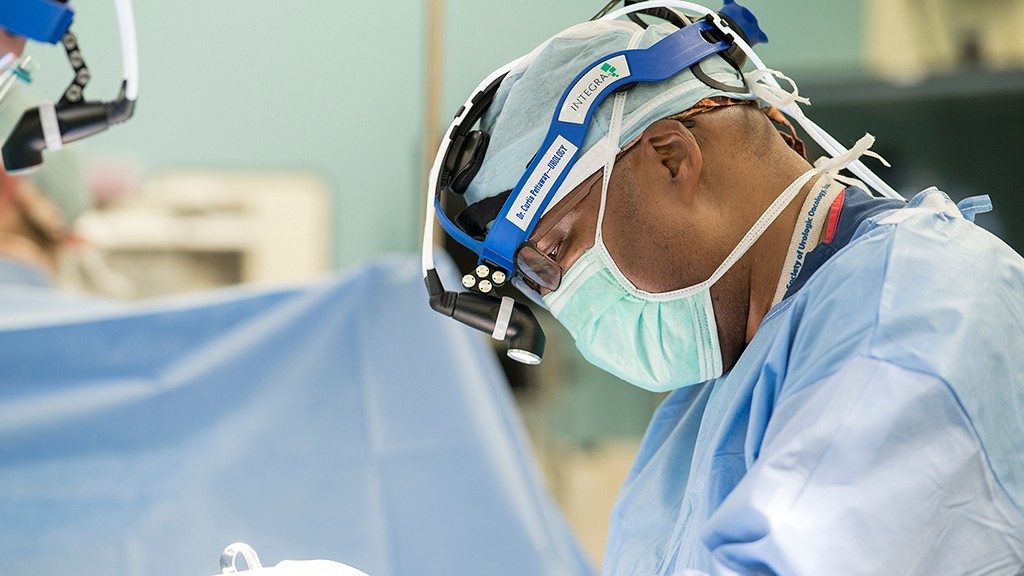 Curtis Pettaway, M.D., performs urologic cancer surgery in the operating room while wearing a face mask and a headlamp.