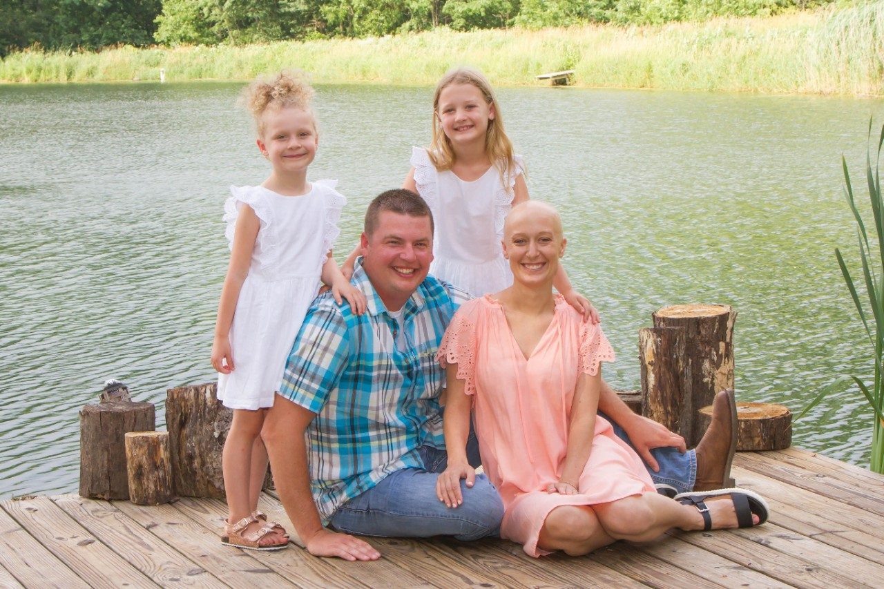 Thymoma survivor Kirsti Hoopingarner sits in front of a lake beside her husband and two daughters.