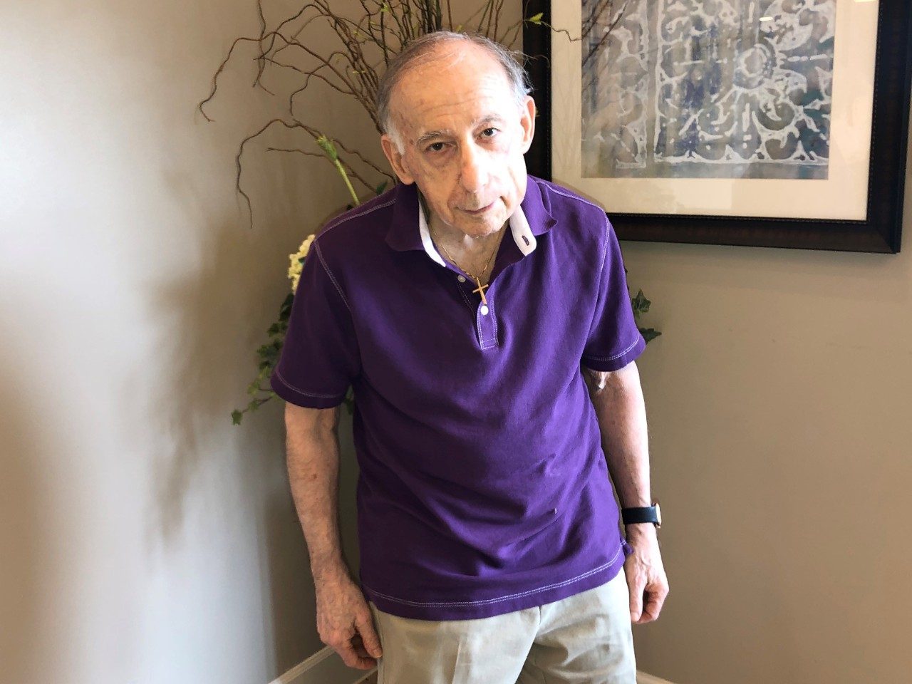 Merkel cell carcinoma survivor Arthur Sulkin wears a purple shirt and stands in front of a plant