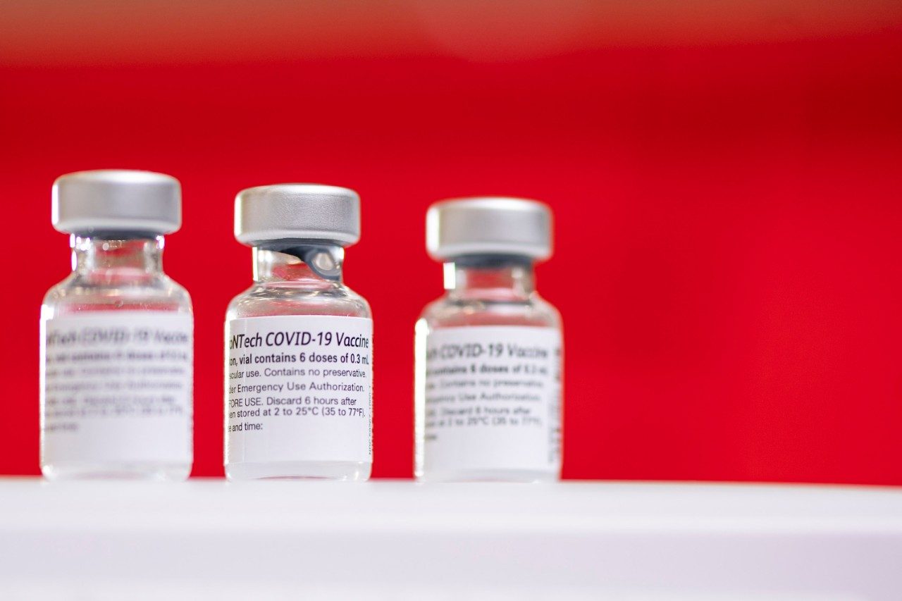 Three COVID-19 vaccine vials against a red background