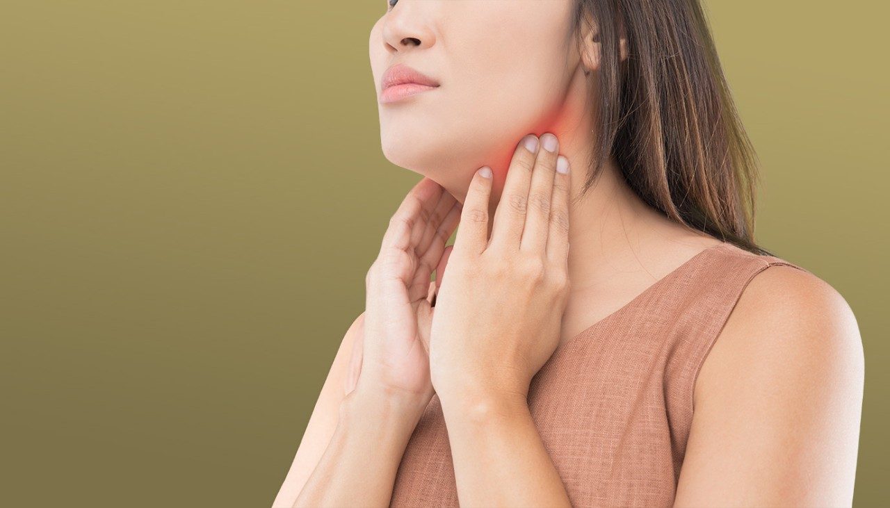 Concerned Asian woman with long brown hair uses her hands to feel her swollen neck lymph nodes