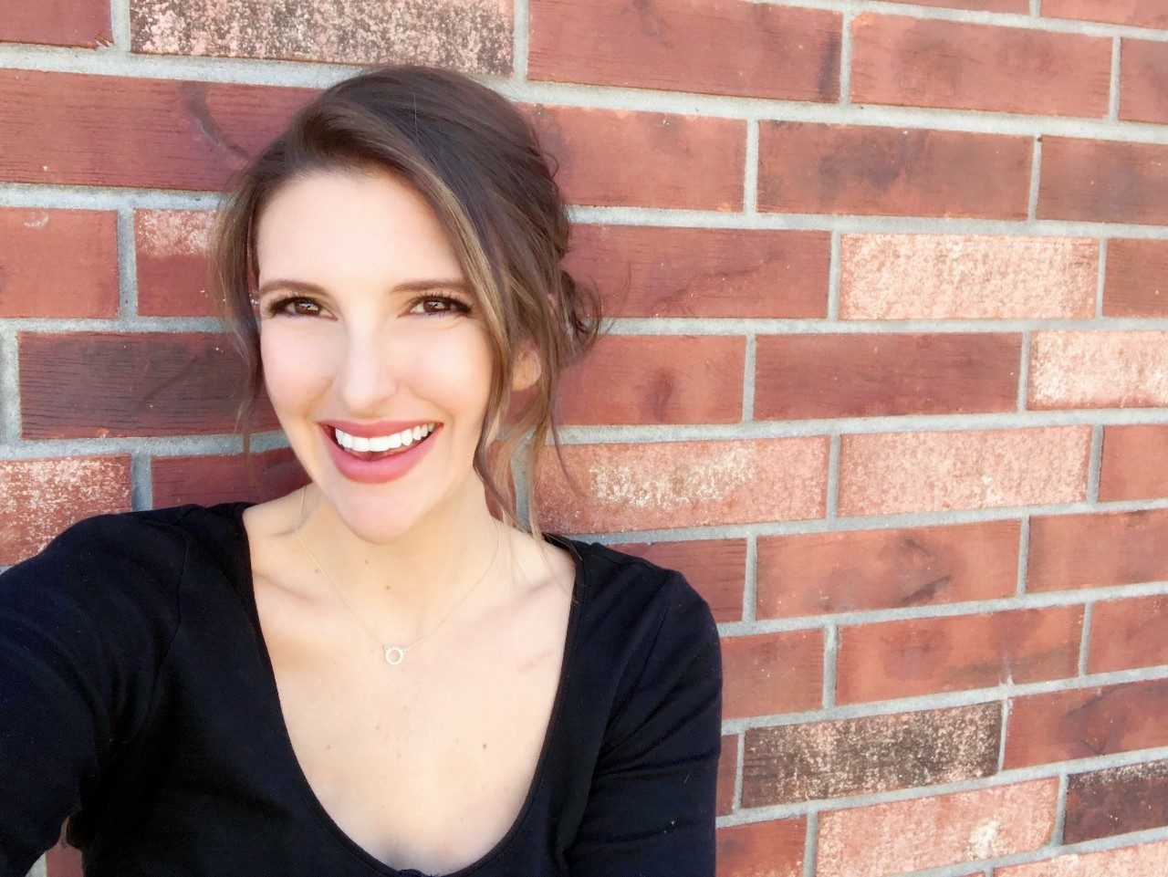 Senior clinical dietitian and breast and ovarian cancer survivor Christie Siebel smiles while standing against a brick wall