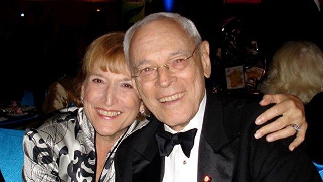 Cancer survivor and caregiver Jane Root, poses with her arm around her late husband, Eli, who is wearing a tuxedo