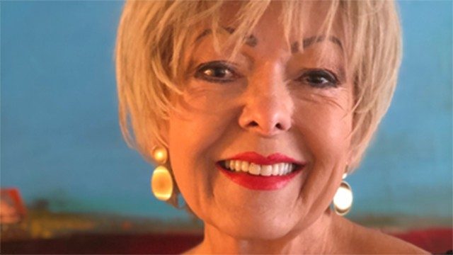 Close-up selfie showing the smiling face of peritoneal mesothelioma survivor Dana Carrera, who has short blond hair and is wearing gold earrings and red lipstick.