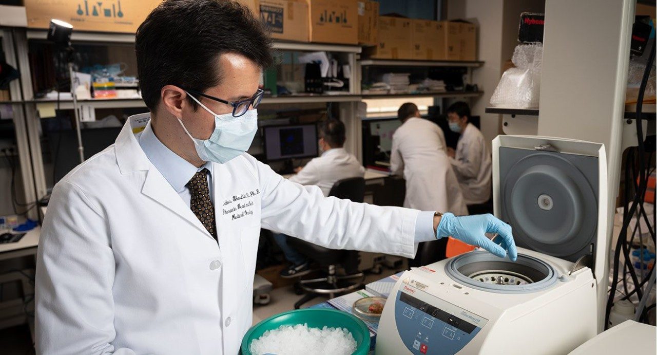 Ferdinandos Skoulidis, M.D., Ph.D., conducting laboratory research while wearing his white coat and medical-grade face mask