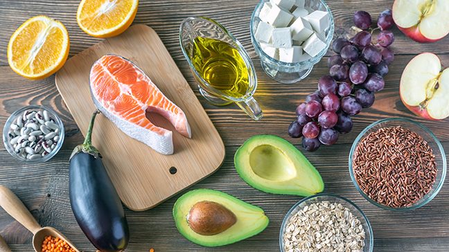 Heart healthy foods on the cardiac diet, including avocado, salmon, tofu, apples, oranges, grapes, oatmeal, oil, eggplant and grains