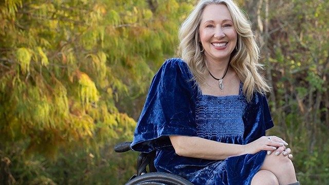 Bladder cancer survivor Karen Roy, seated outdoors in a wheelchair in a blue velvet dress