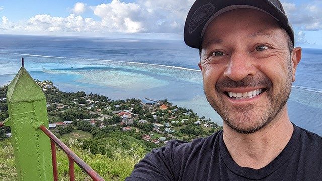 Stage IV colorectal cancer survivor Kris Sokolowski on a hilltop in Bora Bora, with the ocean in the background