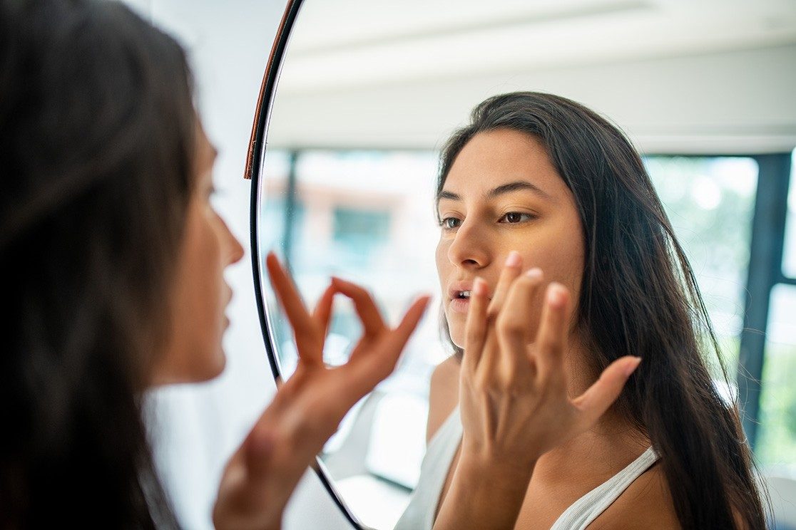 Woman checks skin in a mirror.