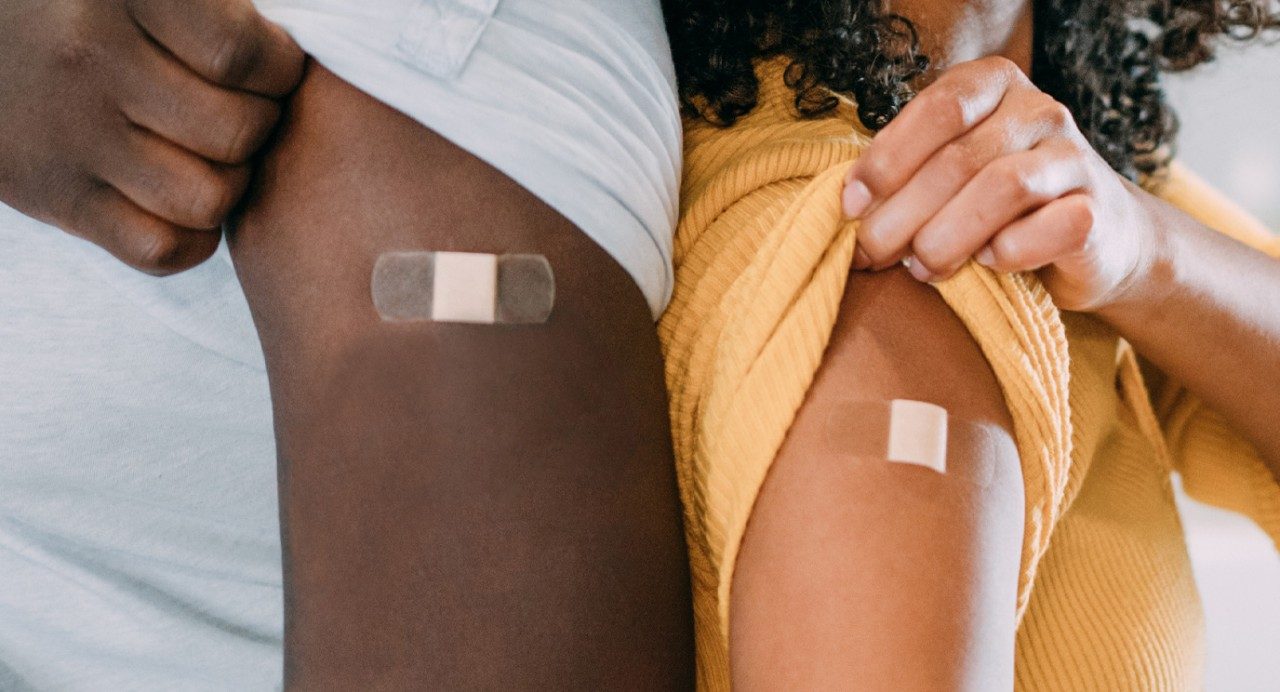 Close-up view of two arms with sleeves rolled up and bandages covering recent vaccinations