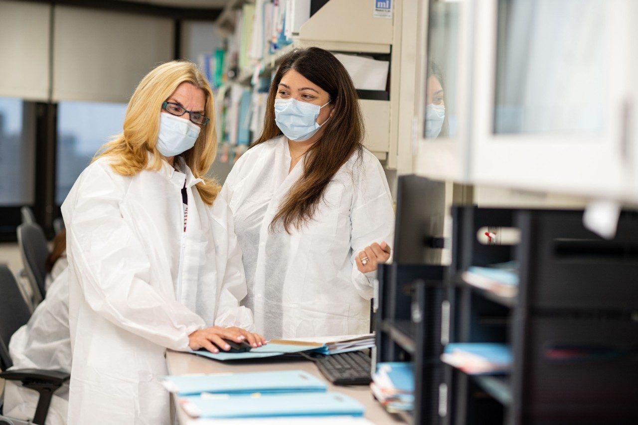 Drs. Elizabeth Shpall and Sairah Ahmed stand next to each other, reviewing a CAR T cell therapy patient's treatment notes.