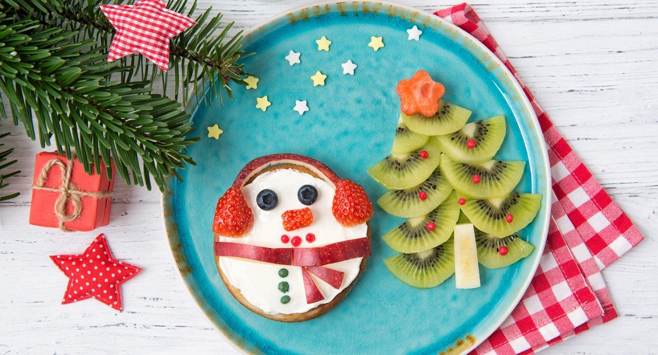 Holiday plate shows snowman cookie and kiwi slices laid out in the shape of a holiday tree.