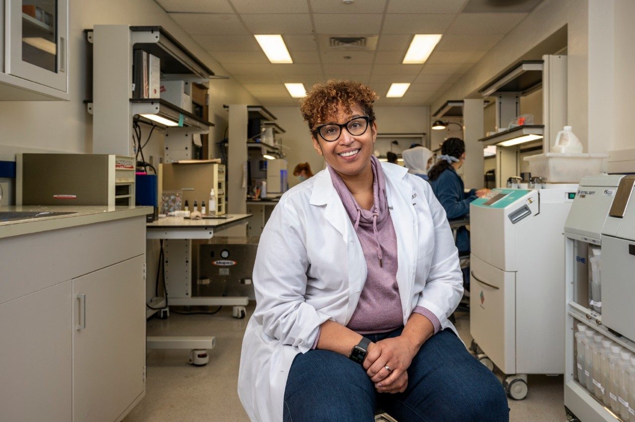 Toysha Mayer, D.H.Sc., sits and poses in the lab while students work behind her in November 2022.