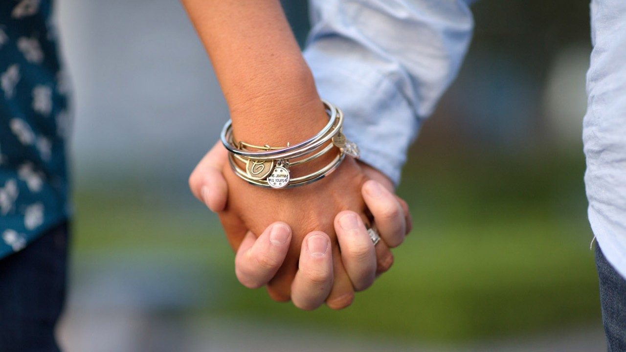 Close up of pale-skinned man and woman's hands clasped together while walking outdoors