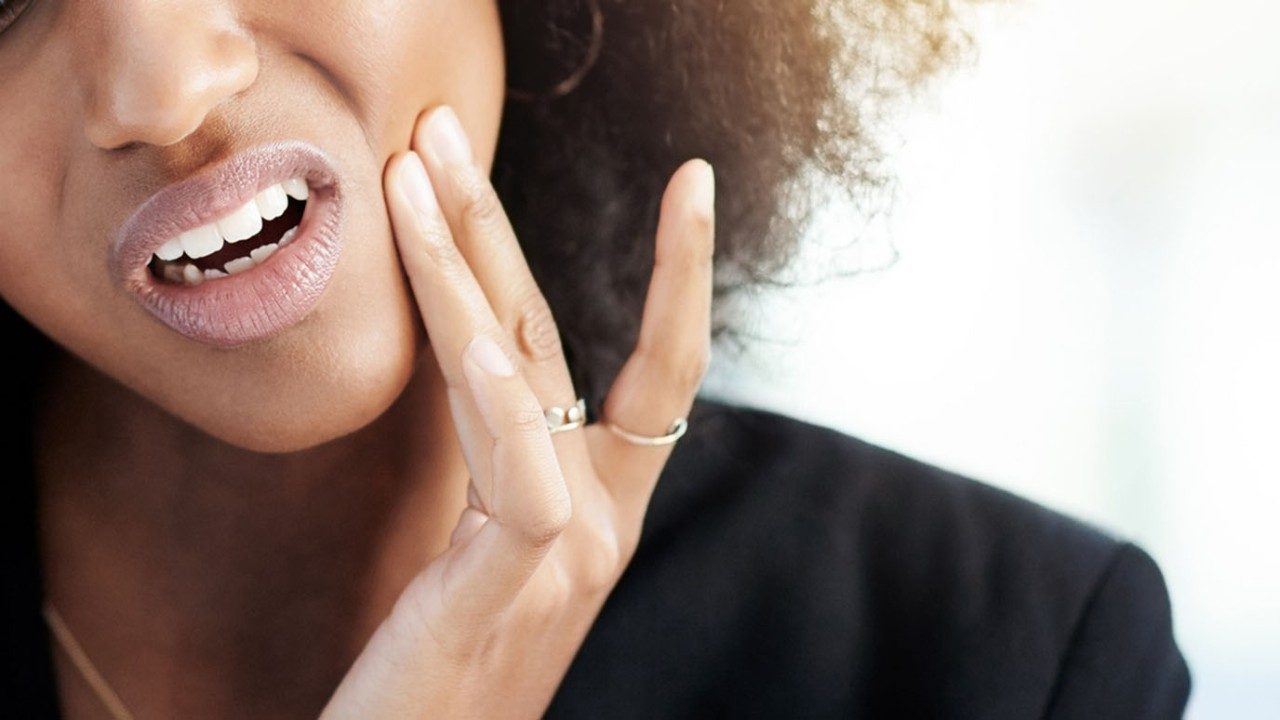 Close-up photo of young Black woman touching the side of her jaw in pain 