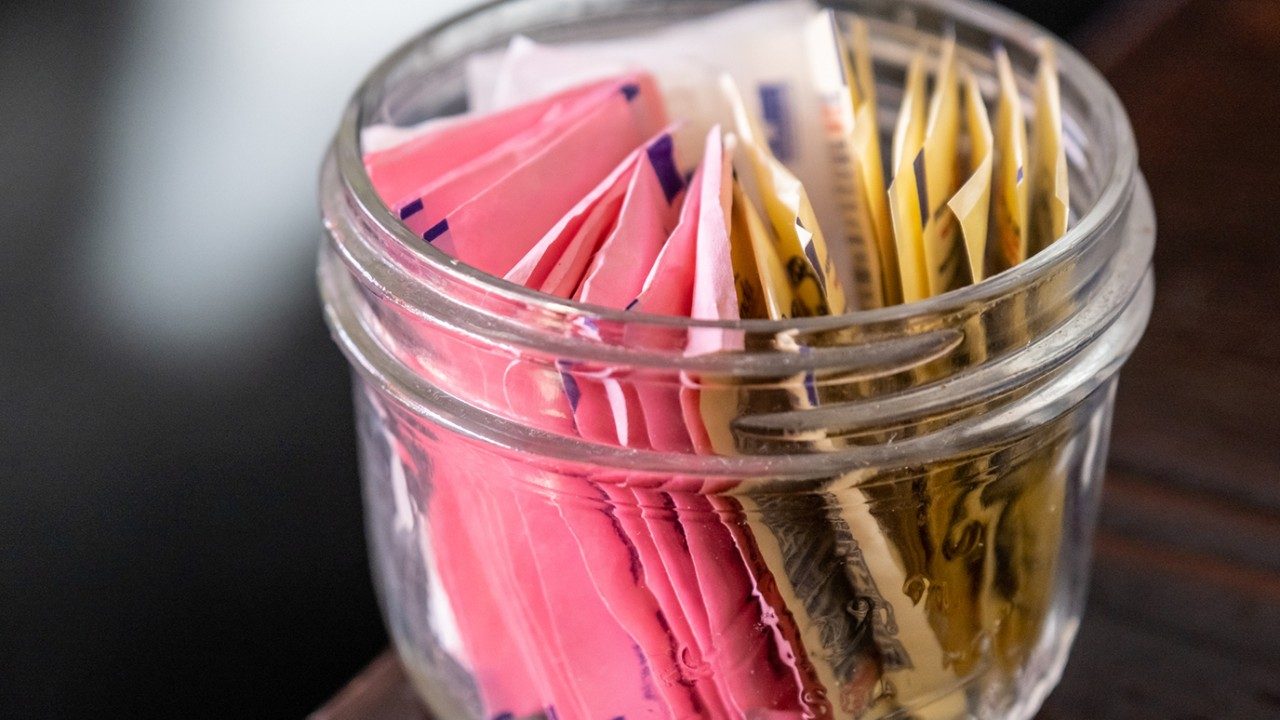 Glass jar containing several types of sweeteners in packets