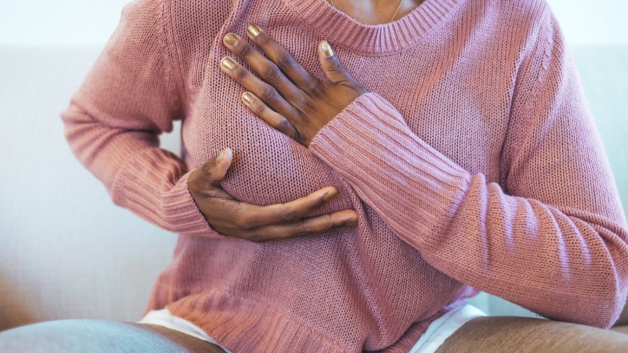 A woman is pictured cupping her right breast, feeling for abnormalities