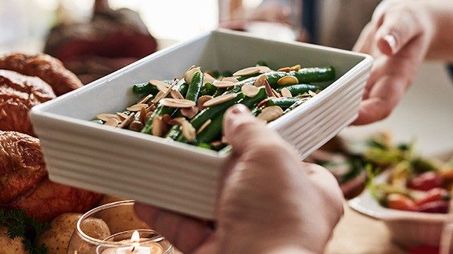 Hand holding white dish with green beans and sliced almonds.