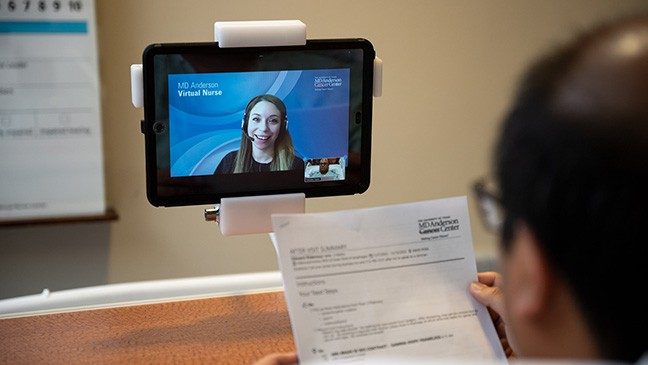 Nurse Christian Perez is shown on a tablet speaking to a patient holding papers with an after-visit summary.