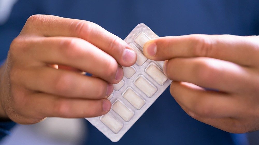 Person in blue shirt holds a packet of white gum in a silver foil package