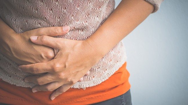 Close-up waist view of woman's hands holding her abdomen in pain