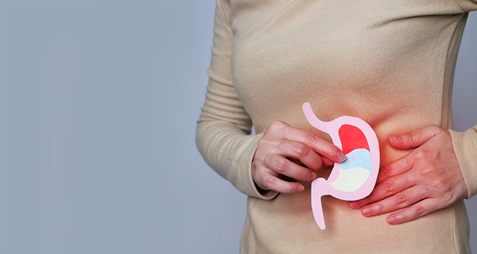 Torso view of woman in beige sweater holding stylized paper stomach in front of abdomen