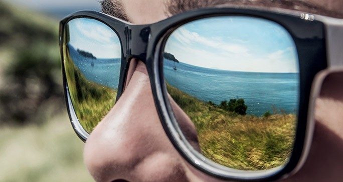 Close-up of mirrored sunglasses reflecting pretty sea coast view