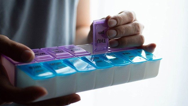 Hands holding a daily pill organizer with blue a.m. and purple p.m. containers