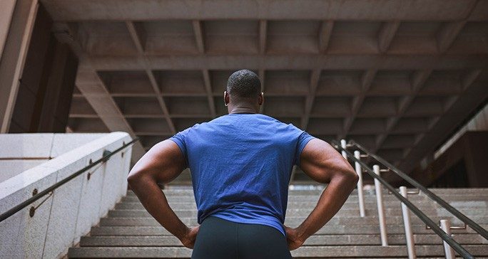 Rear view of muscular Black man in athletic attire looking up stadium steps