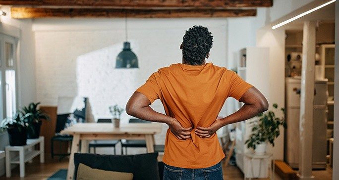 Rear view of Black man in a burnt orange T-shirt and jeans holding his back in pain