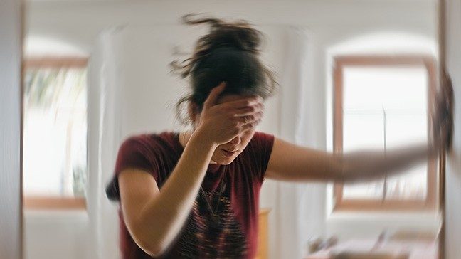 Woman holding her forehead in pain and leans against a wall