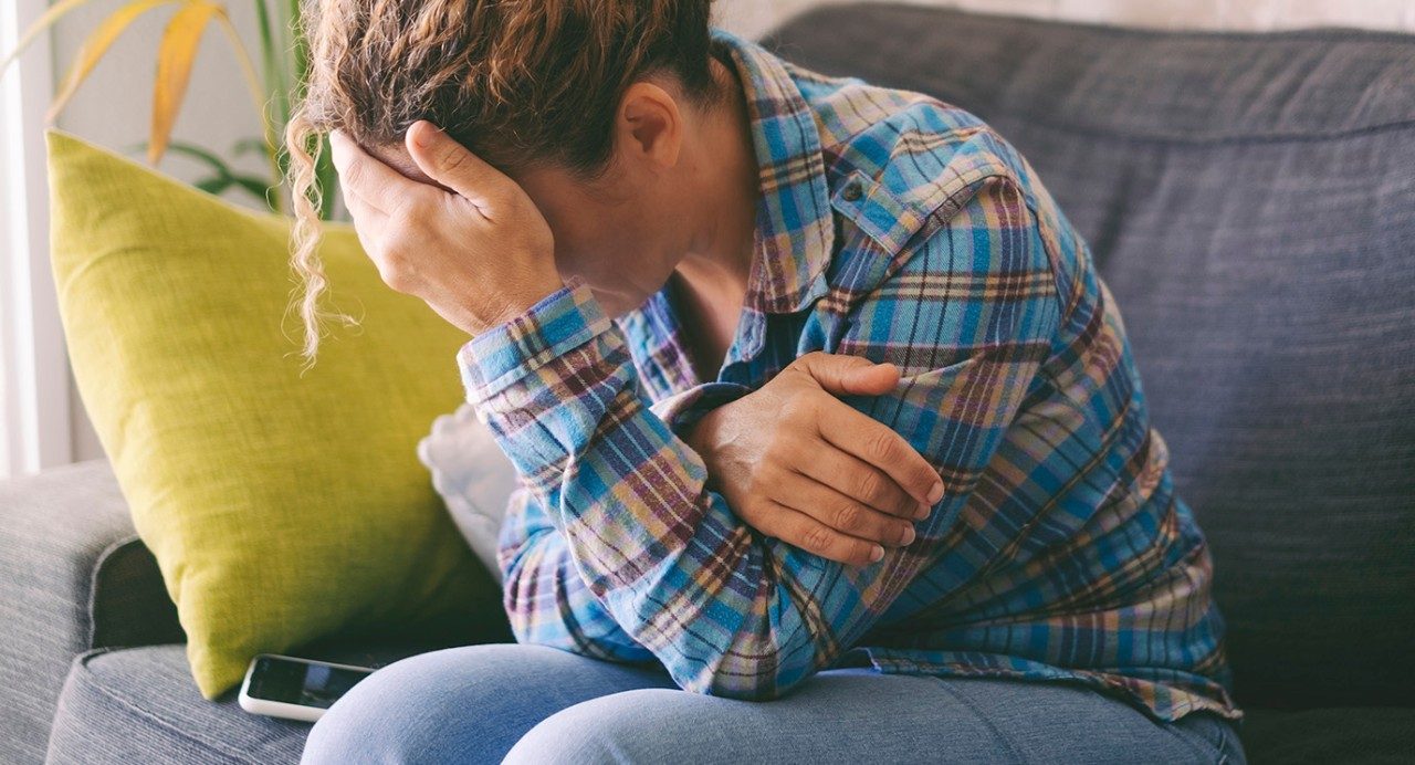 Unidentifiable distressed woman holds head in hand on couch