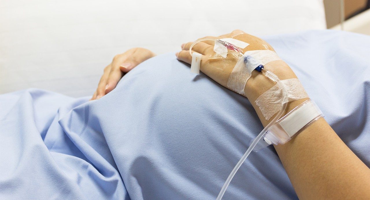 Close-up of pregnant belly in hospital gown with IV in arm