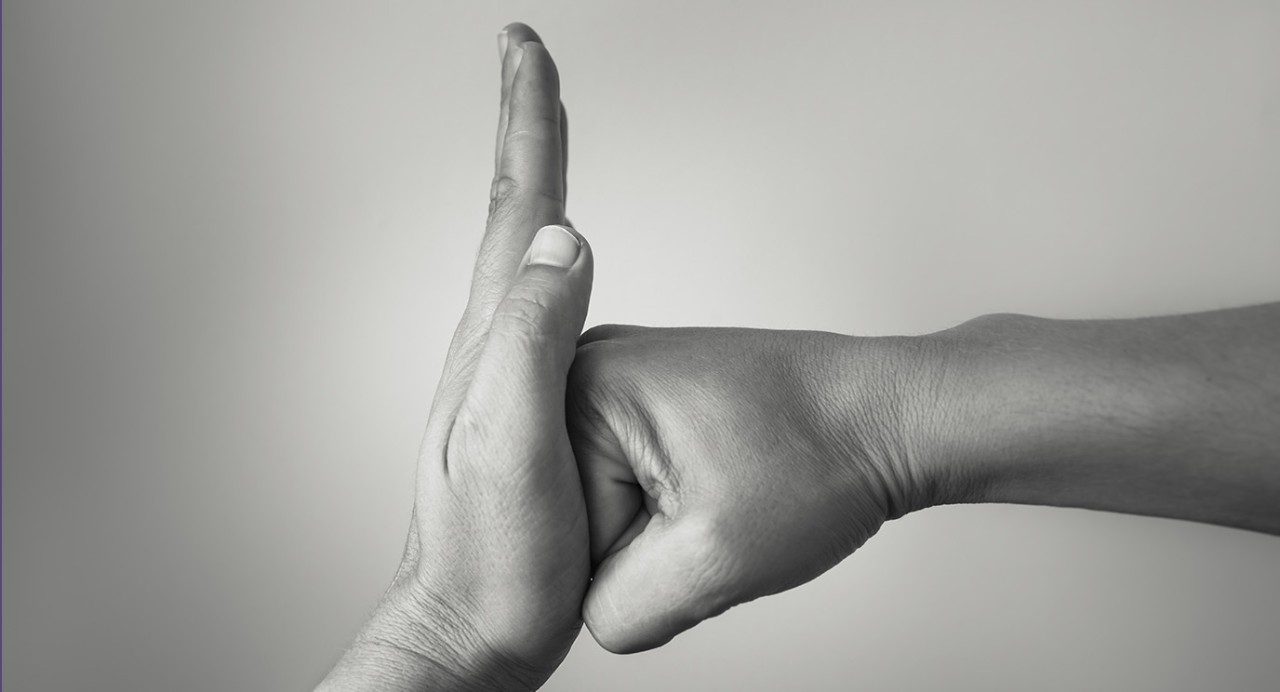 Black-and-white close-up of one hand in a "stop" position, blocking a closed fist