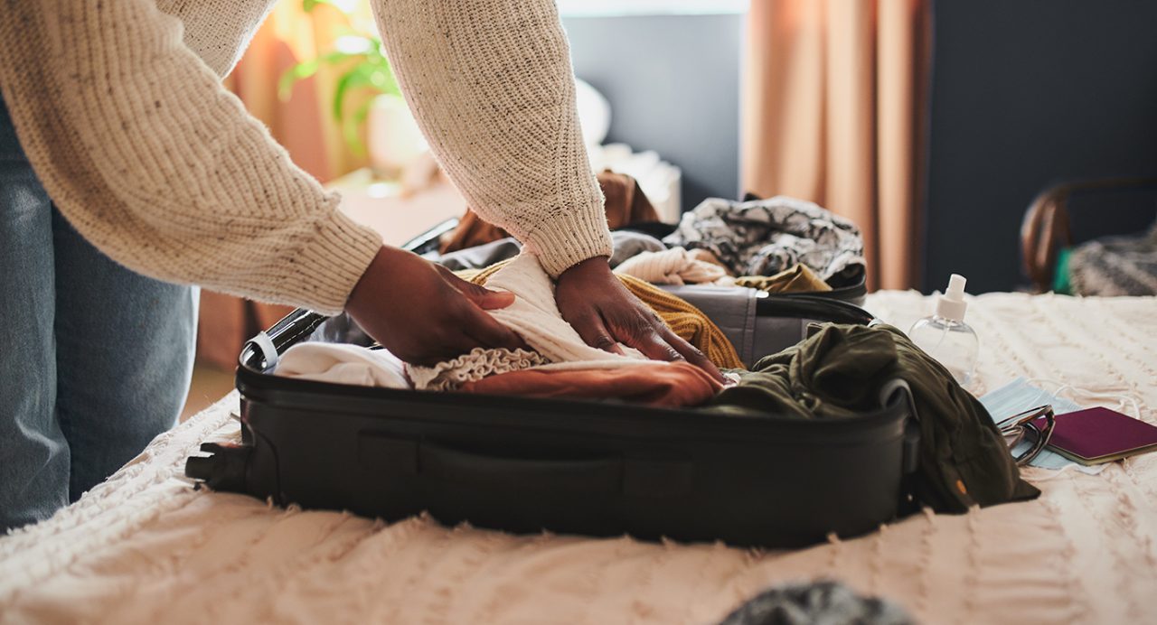 Close-up of a Black woman's hand packing a suitcase with clothing