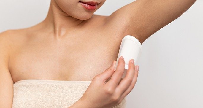 Torso view of towel-wrapped woman applying anti-perspirant