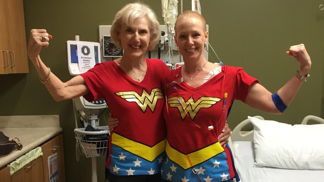 Kristy Mouton and her mother stand and flex their arms in Wonder Woman shirts.